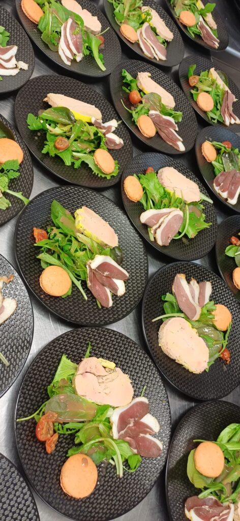 Assiettes individuelles avec mesclun, foie gras, tranches de magret de canard, macaron salé et tomates confites, préparées par Kameleon Traiteur.