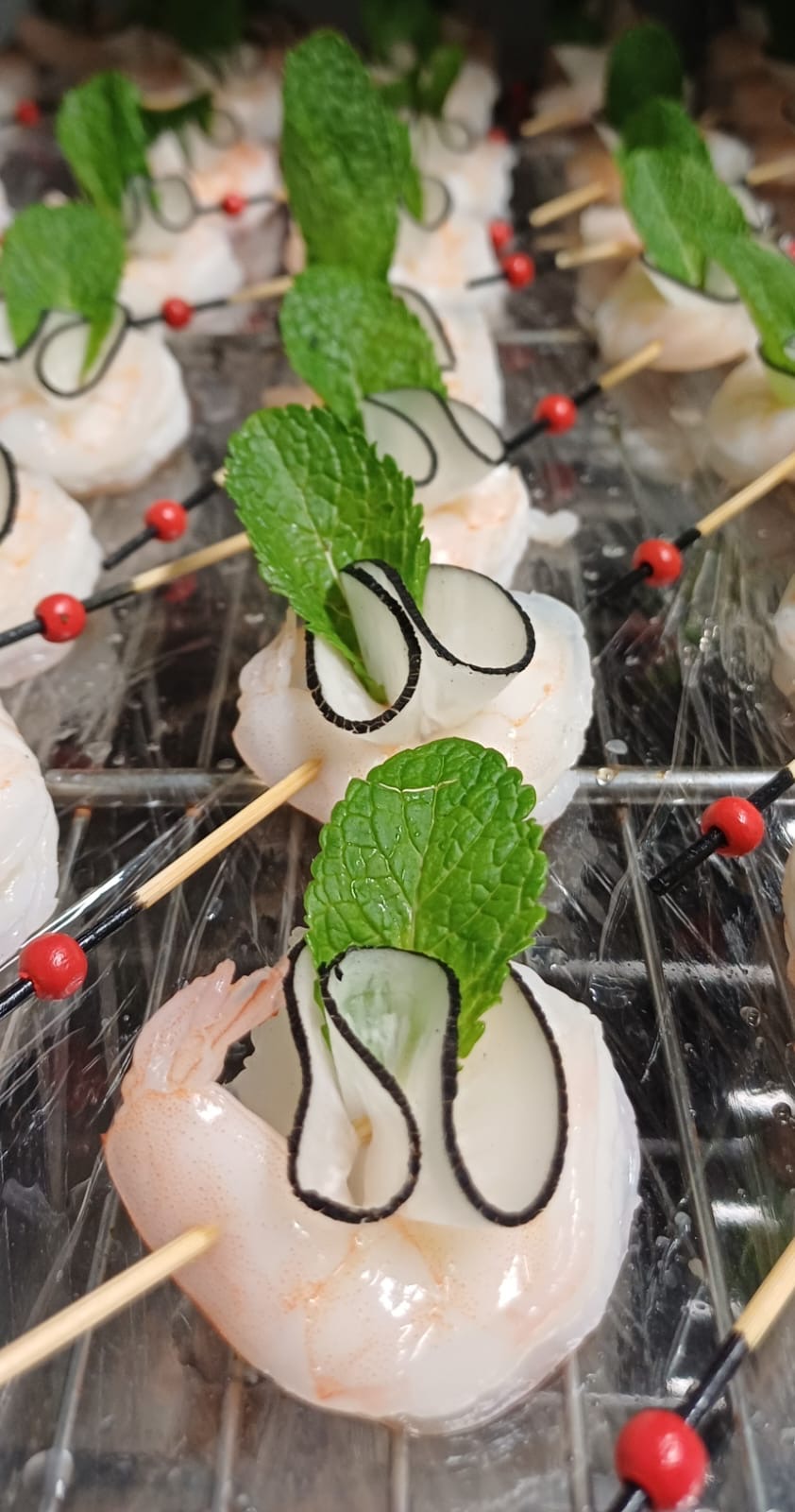 Brochettes apéritives de crevettes avec rubans de concombre et feuille de menthe, dressées pour un cocktail par Kameleon Traiteur.